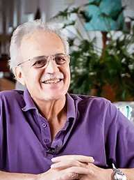 Carlos Nobre de óculos e camisa polo roxa sorrindo